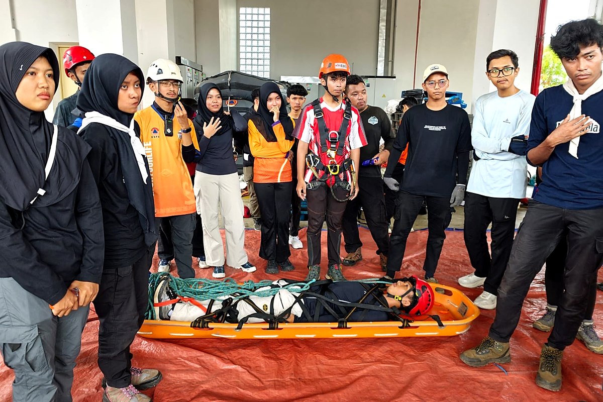 Sejumlah peserta berhelm dan berharness berdiri mengelilingi korban uji yang dibaringkan di tandu di atas terpal merah