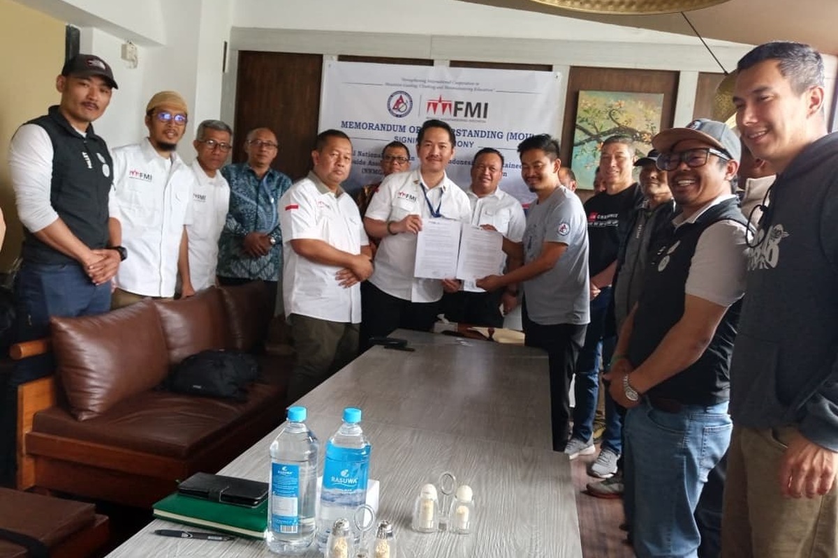 Sekelompok peserta berdiri berjajar memegang naskah bertanda tangan di depan latar acara penandatanganan FMI dan NNMGA